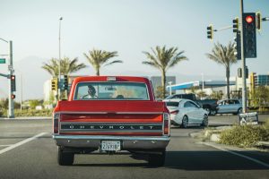 Red vintage Chevrolet truck at traffic light in Los Angeles street backdrop with palm trees.